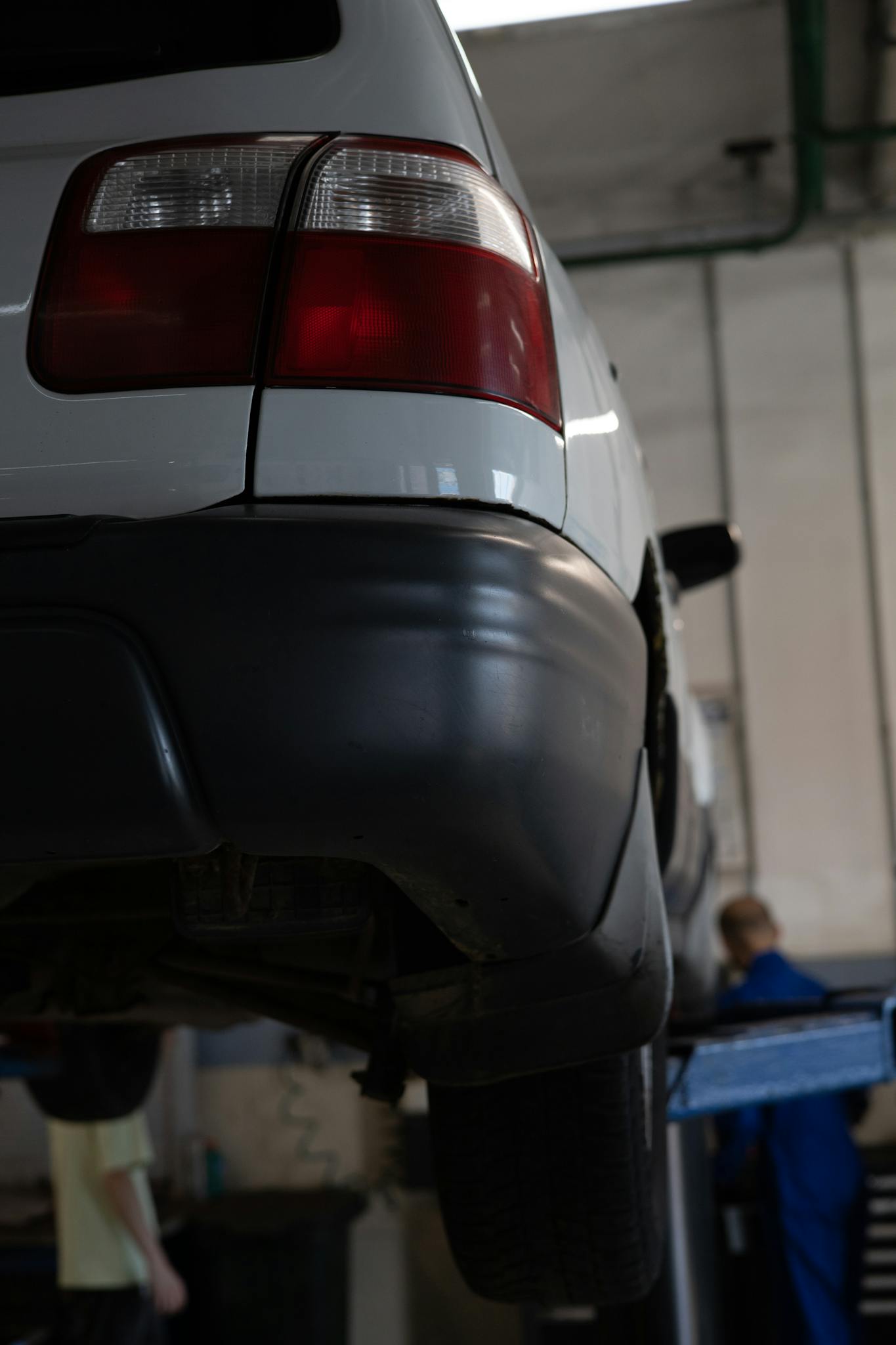 Close-up of a car in a workshop for maintenance, displaying a taillight and mechanic.