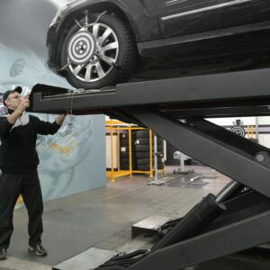 Mechanic carefully examining car on hydraulic lift in automotive workshop, ensuring safety and performance.