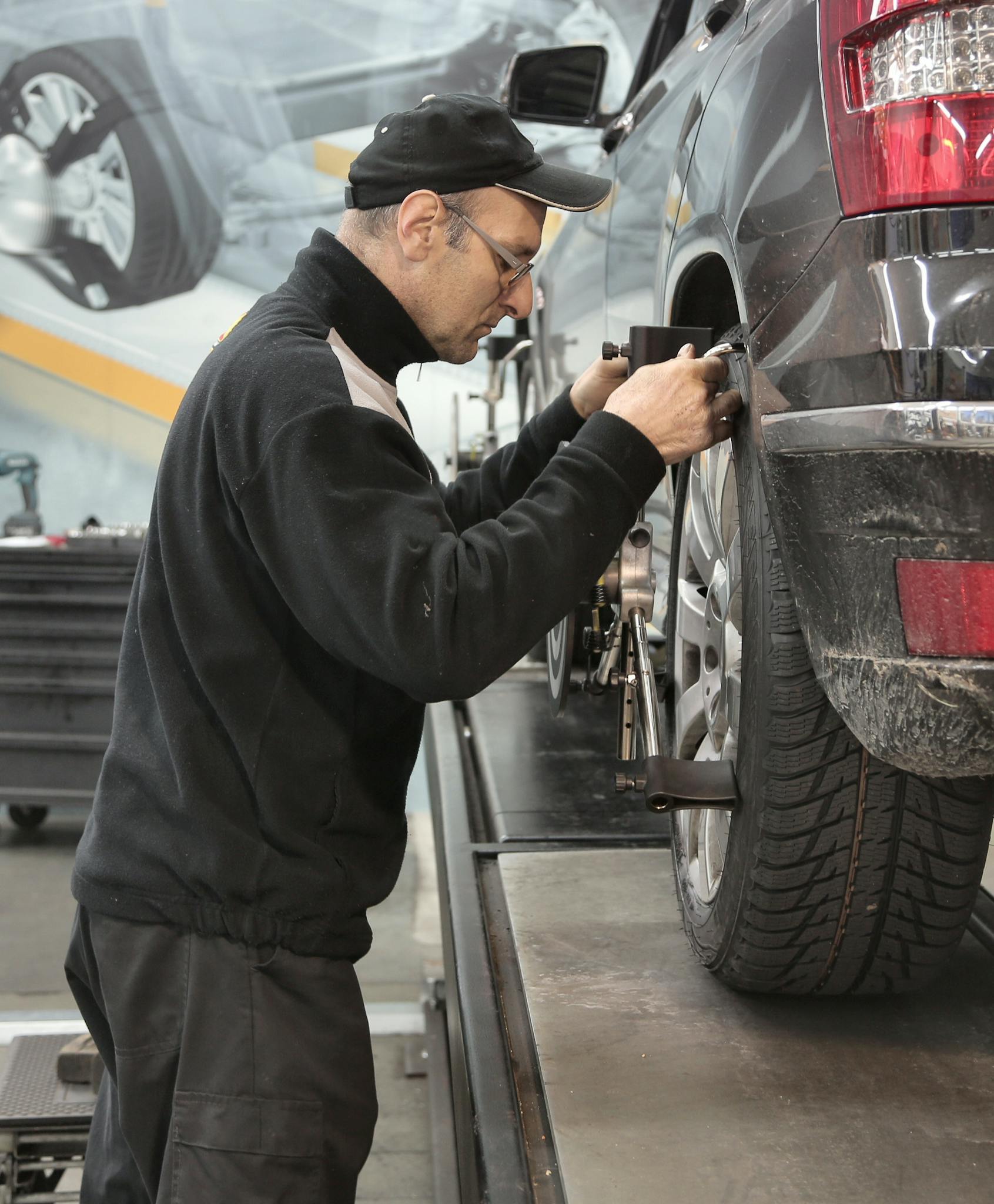 Side view of a mechanic aligning a car tire in a professional auto workshop.